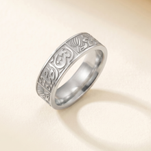 Silver ring with intricate design on a beige background